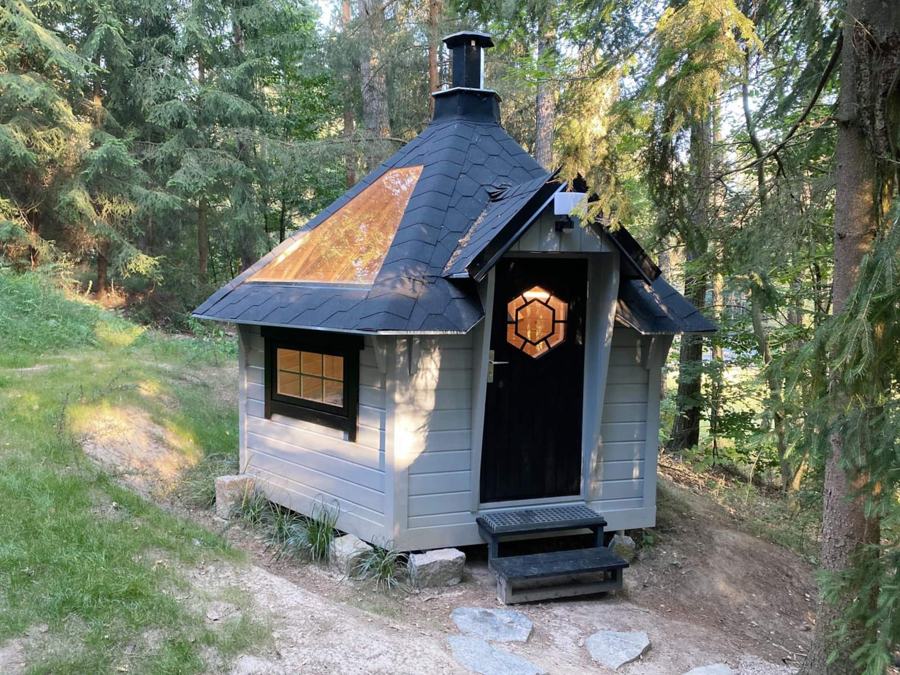 Šedý šestiboký grilovací domek s komínem na lesní mýtině