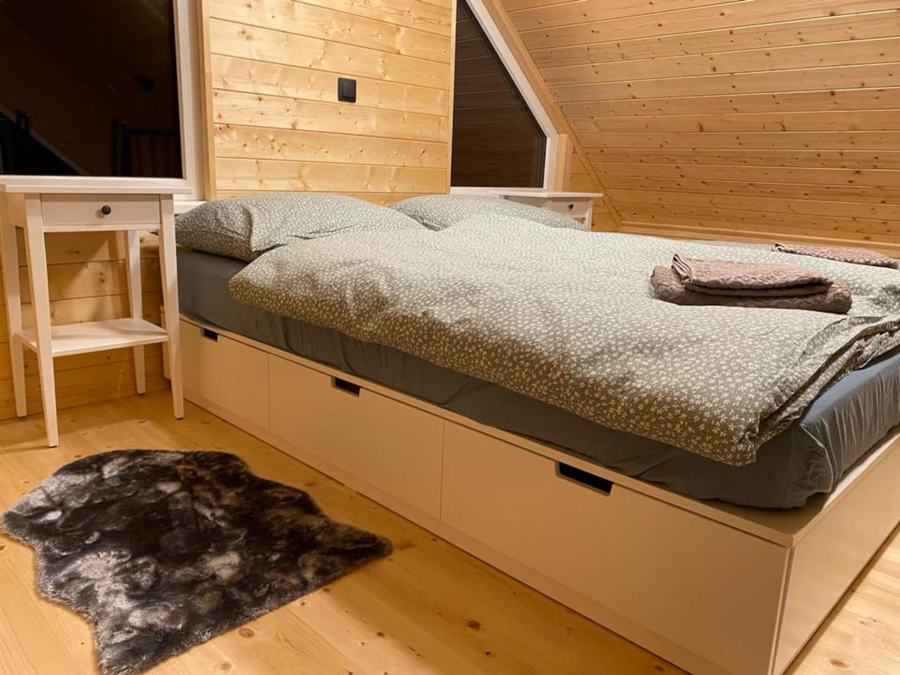 Postel s úložnými šuplíky pod šikmou dřevěnou střechou, na podlaze kožešina
